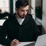 A focused young man using a laptop at a desk in a stylish home office setting.