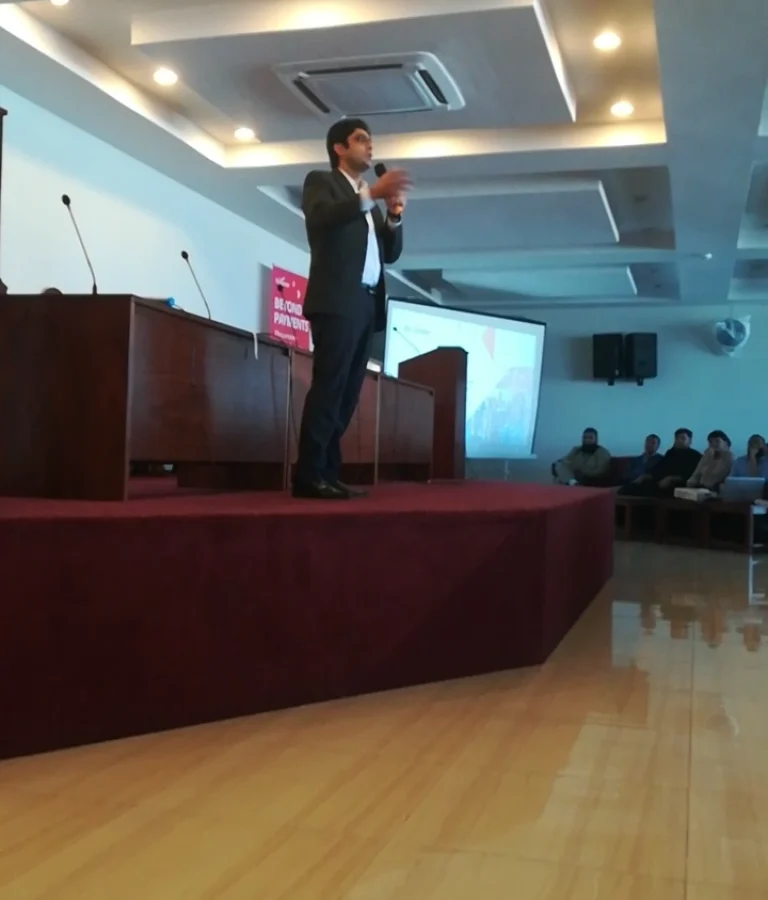 Atif speaking at a Payoneer seminar, standing on stage with presentation screen and audience.